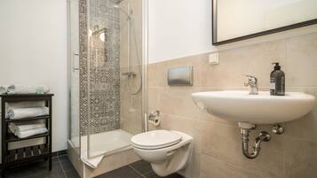 A bathroom with a shower, toilet, sink, and a towel rack.