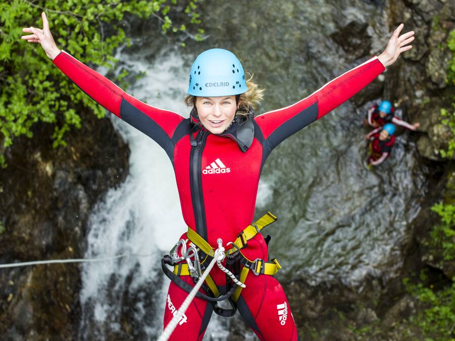 A person bungee jumping with safety harnesses and a helmet, with a rocky waterfall in the background.