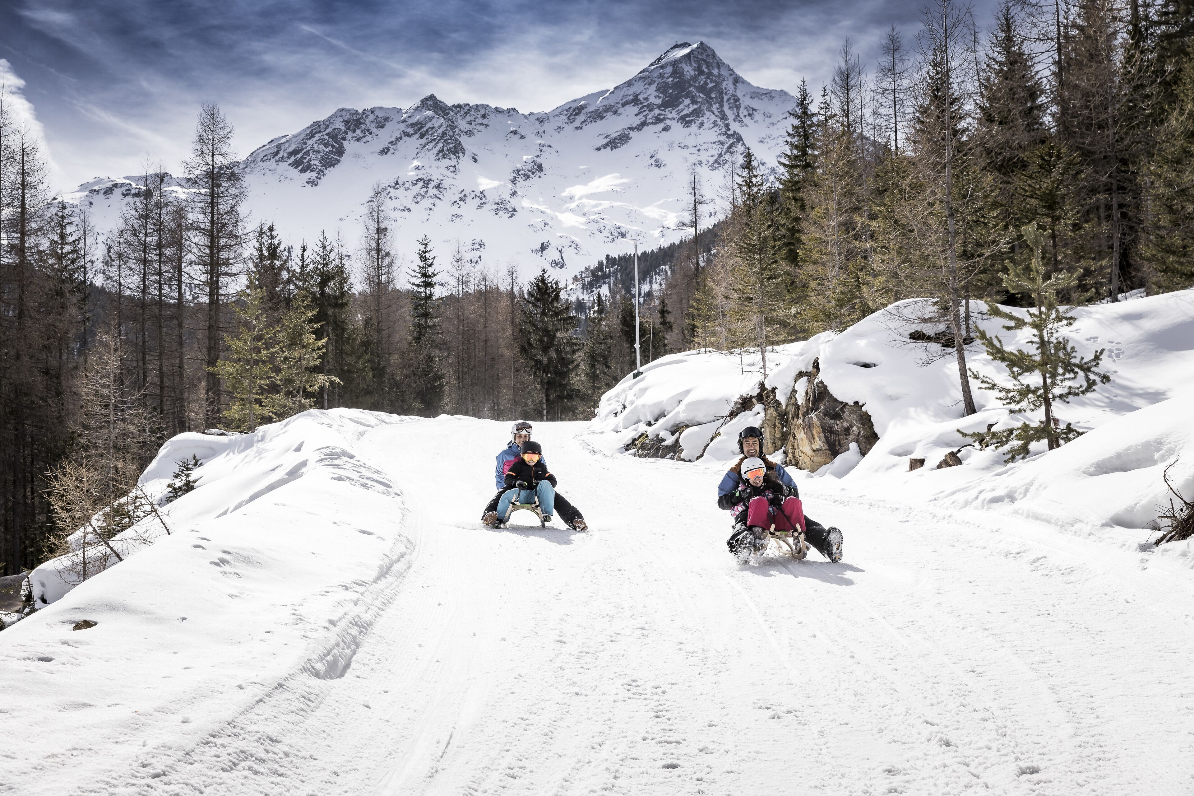A snowy mountain path with two people sledding.