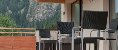 Un área de estar moderna al aire libre con una terraza de madera, sillas metálicas y vistas a un paisaje montañoso.