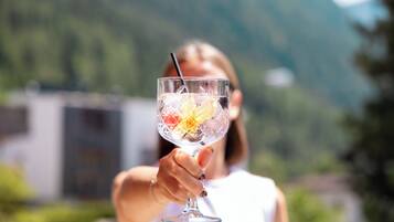 Una persona sosteniendo un vaso transparente con pajita, que contiene una bebida y rodajas de fruta, al aire libre con una montaña y un edificio de fondo.