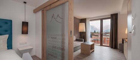 Un hotel moderno con una cama grande, una puerta corredera de madera, un escritorio y vistas a las montañas.
