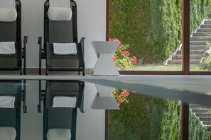 Una habitación con un ventanal amplio, el reflejo de sillas y vista a un jardín con una escalera.