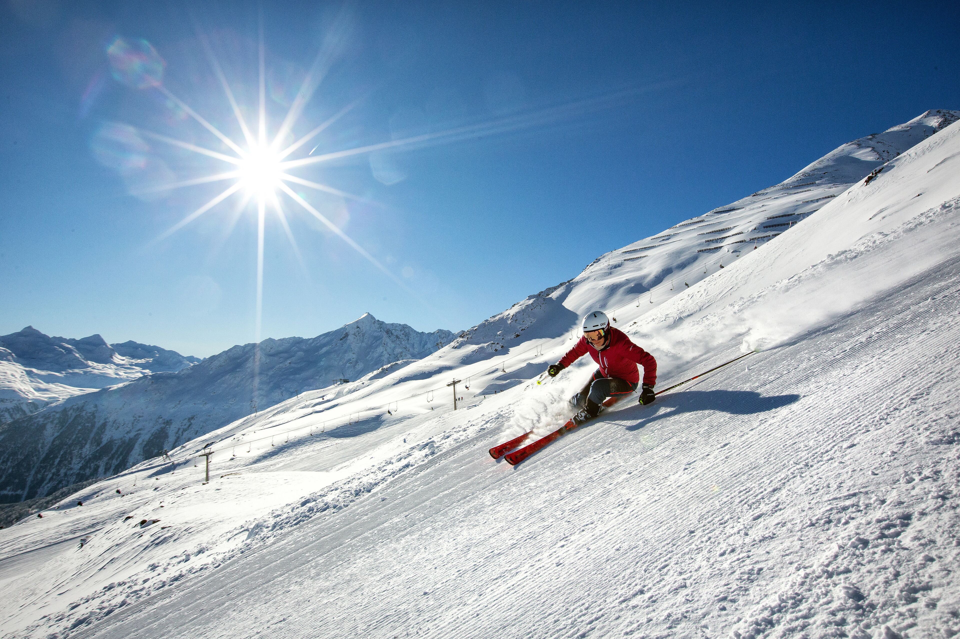 A skier on a snowy slope with mountains in the background and a clear sky.