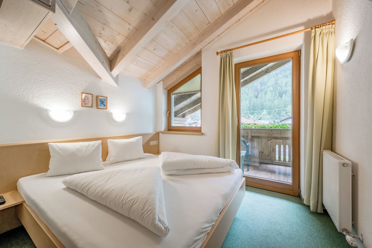 Una cama bien tendida con sábanas blancas, cabecera de madera y una ventana con cortinas.