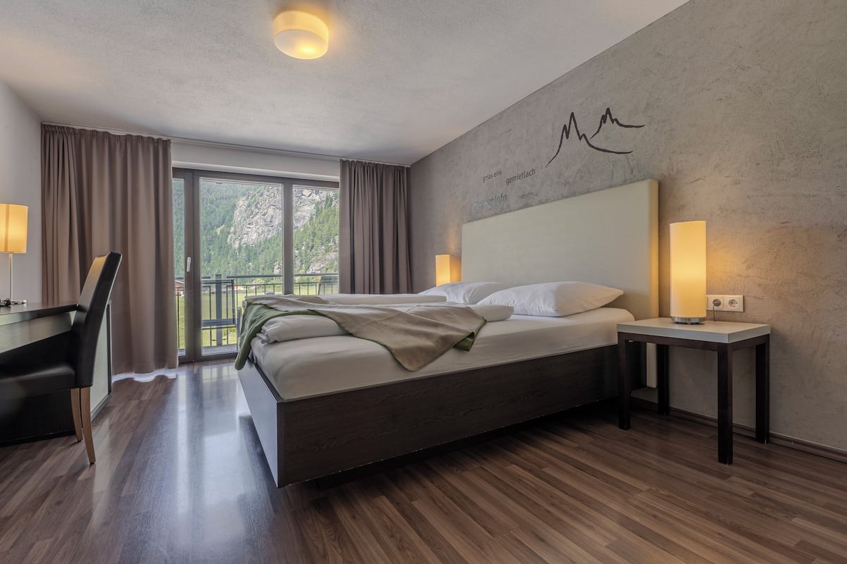 Habitación de hotel moderna con una cama grande, un escritorio y un balcón con vistas al exterior.
