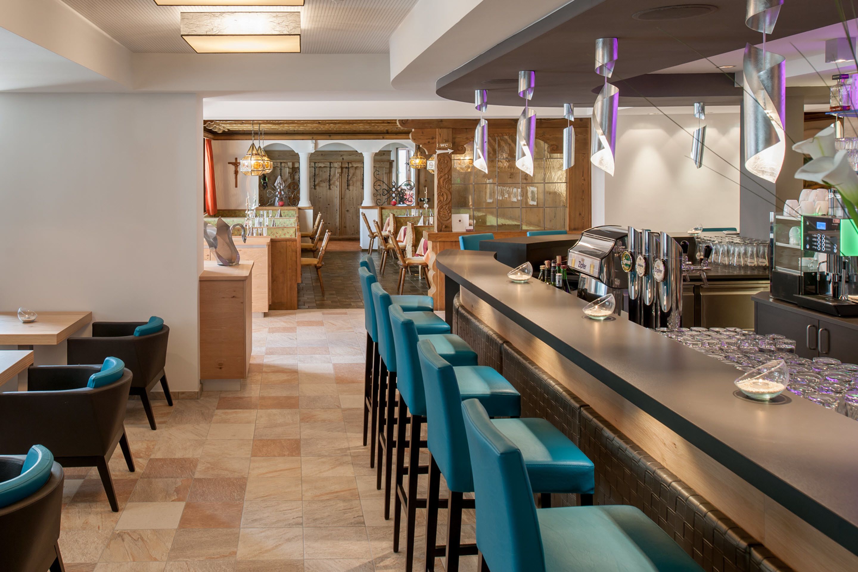 Zona de bar con una barra larga, varios taburetes y una máquina de café.