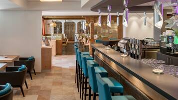 Zona de bar con una barra larga, varios taburetes y una máquina de café.