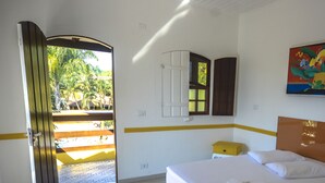 A hotel room with a bed, a small bedside table, a mirror, and a door leading to an outdoor area. - Pousada Praia do Jabaquara (Paraty)