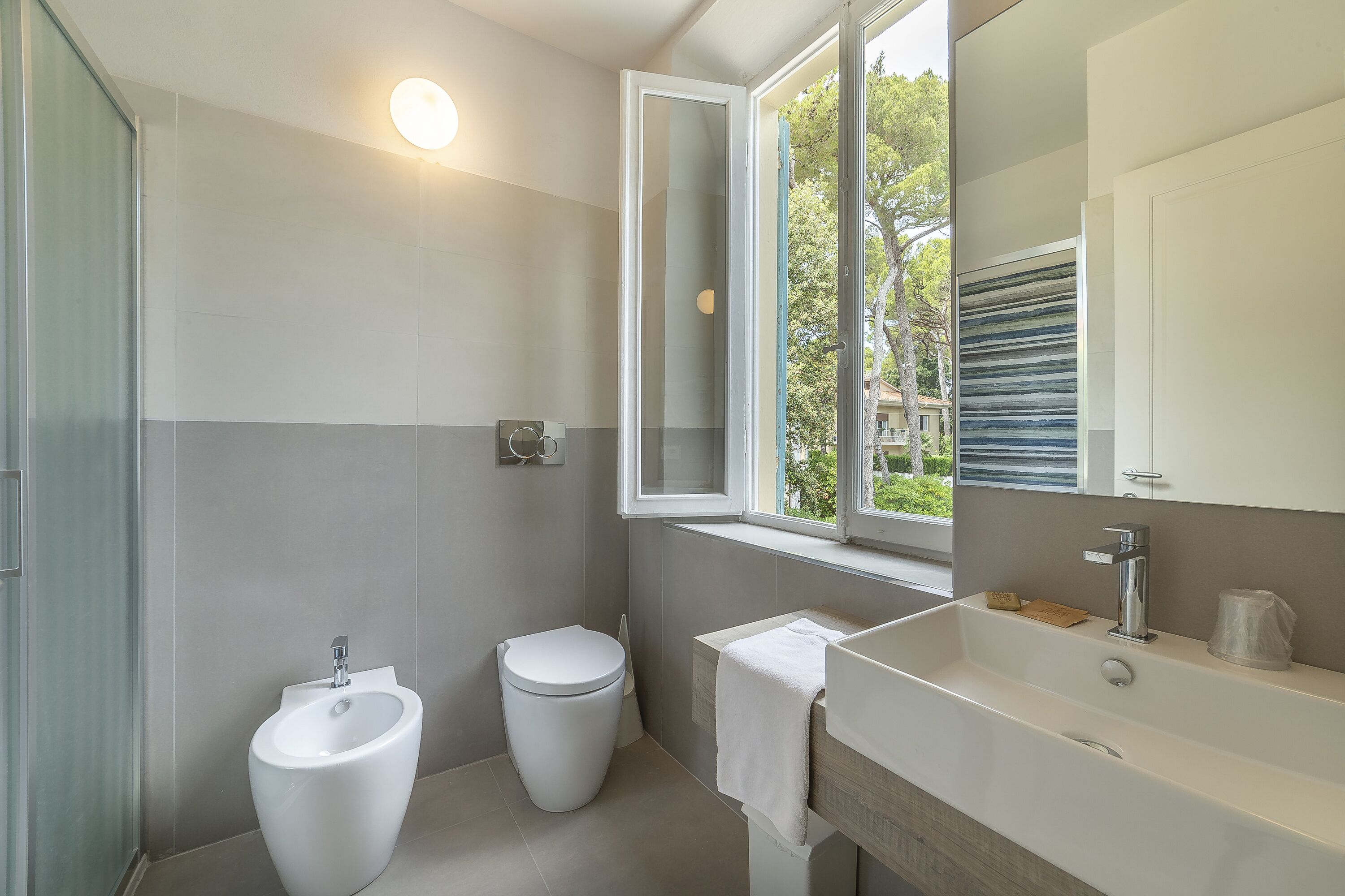Un baño moderno con bidé, inodoro y un lavabo grande con espejo.