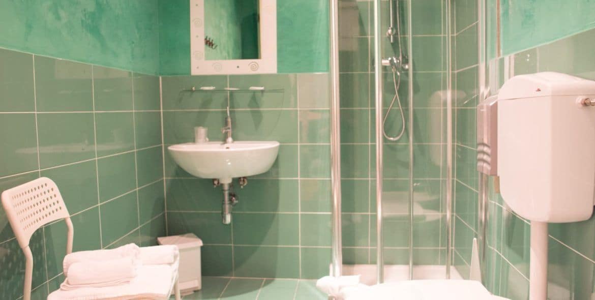 Une salle de bain avec des carreaux verts, un lavabo blanc, une douche et des toilettes blanches.