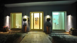 A hotel entrance with three doors, each illuminated by wall-mounted lights. - Guerrini Hotel (Rosignano Marittimo)