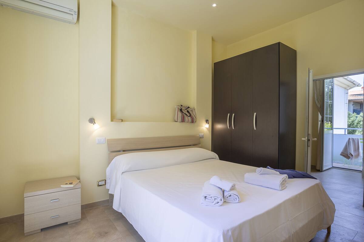 Un dormitorio con cama, armario, mesita de noche y una pequeña cómoda.