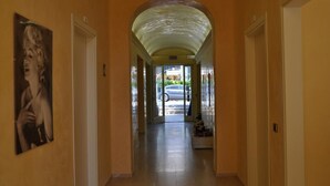 A hallway with a curved ceiling, a painting on the left wall, and a door at the end leading outside. - Guerrini Hotel (Rosignano Marittimo)