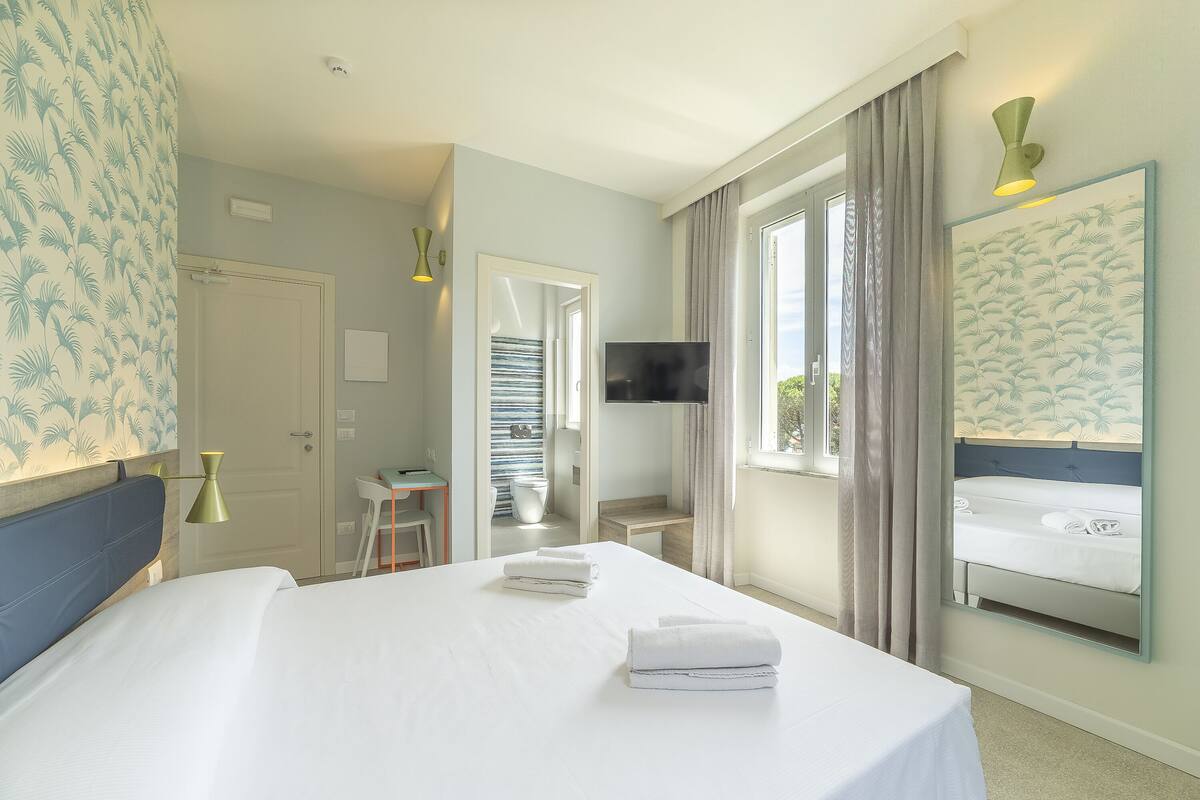 Habitación de hotel con cama, escritorio, televisor y baño visible a través de una puerta abierta.