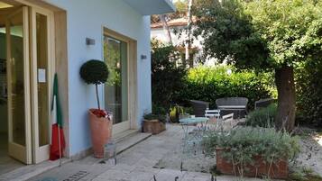 Ingresso di un hotel con porta in vetro, una pianta in vaso, mobili da esterno e un'area giardino.