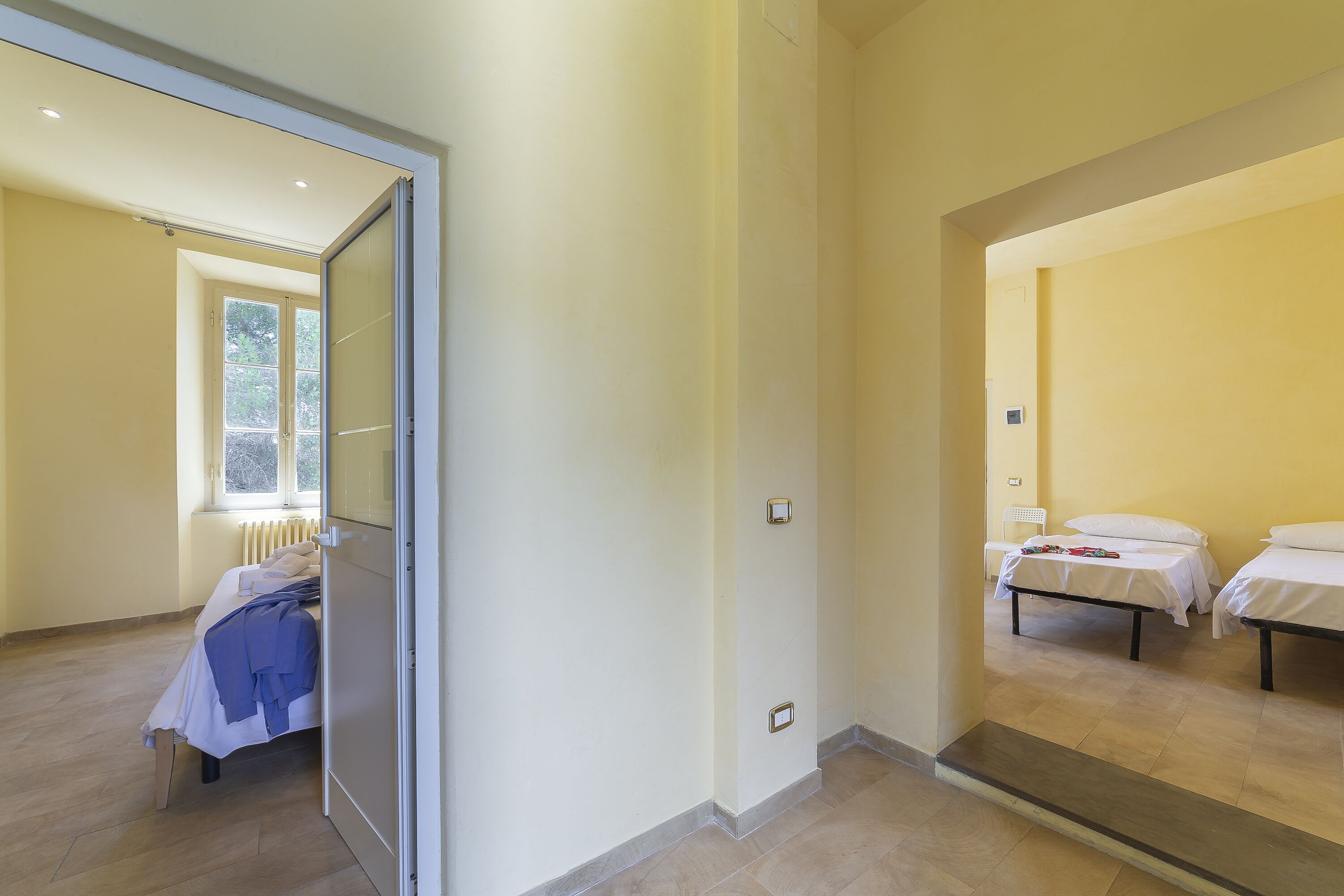 A hotel room with a large sliding door leading to a balcony, a bed with a white comforter, and a bedside table.