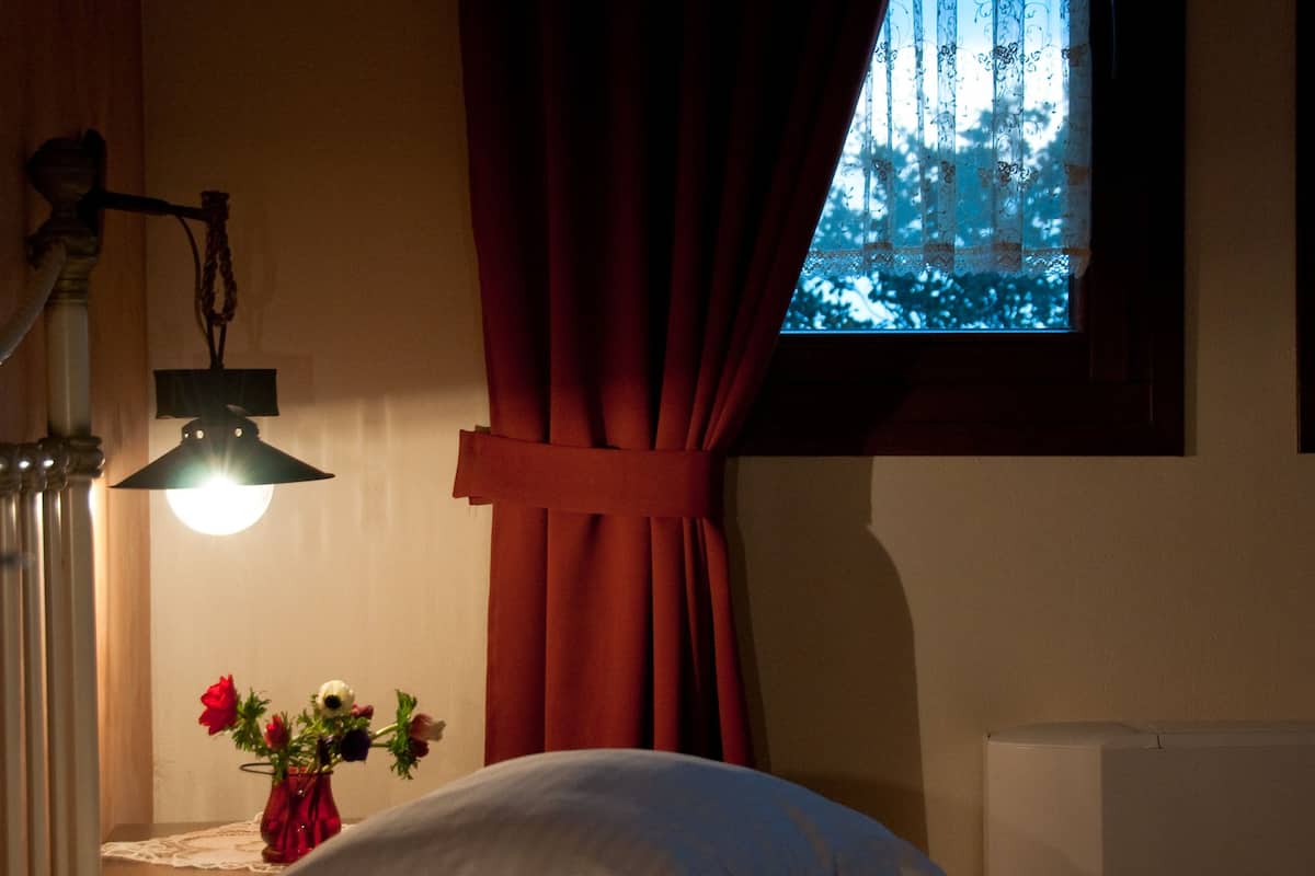 A bedroom with a bed, a nightstand with a lamp, and a window with curtains.