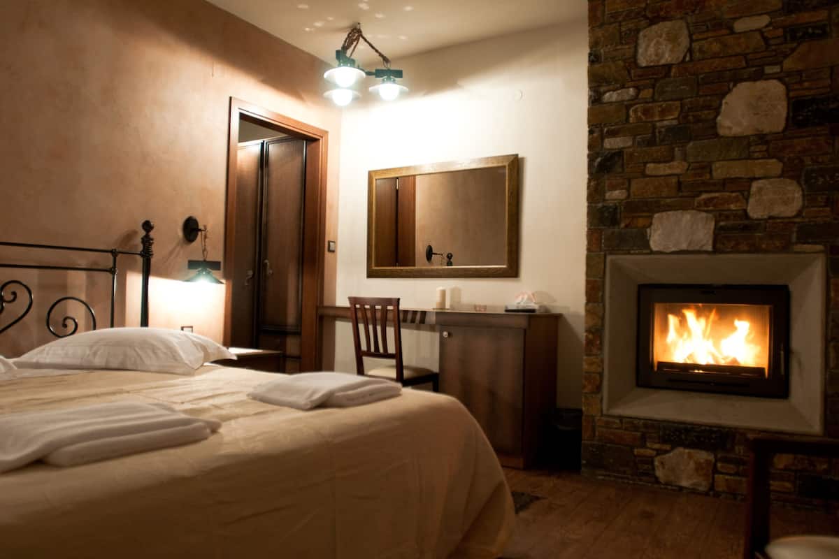 A hotel room with a bed, a desk, a chair, a fireplace, and a mirror.