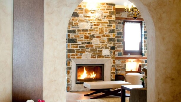 A cozy living room with a stone fireplace, a wooden bench, and a vase with flowers. - Belina Hotel (Volos)