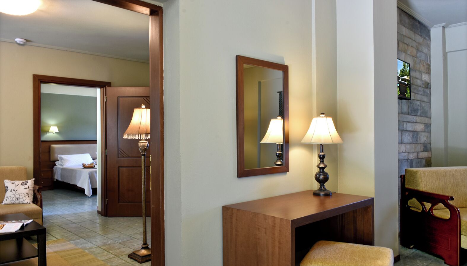 A hotel room with a bed, a desk with a lamp, a chair, and a mirror on the wall.
