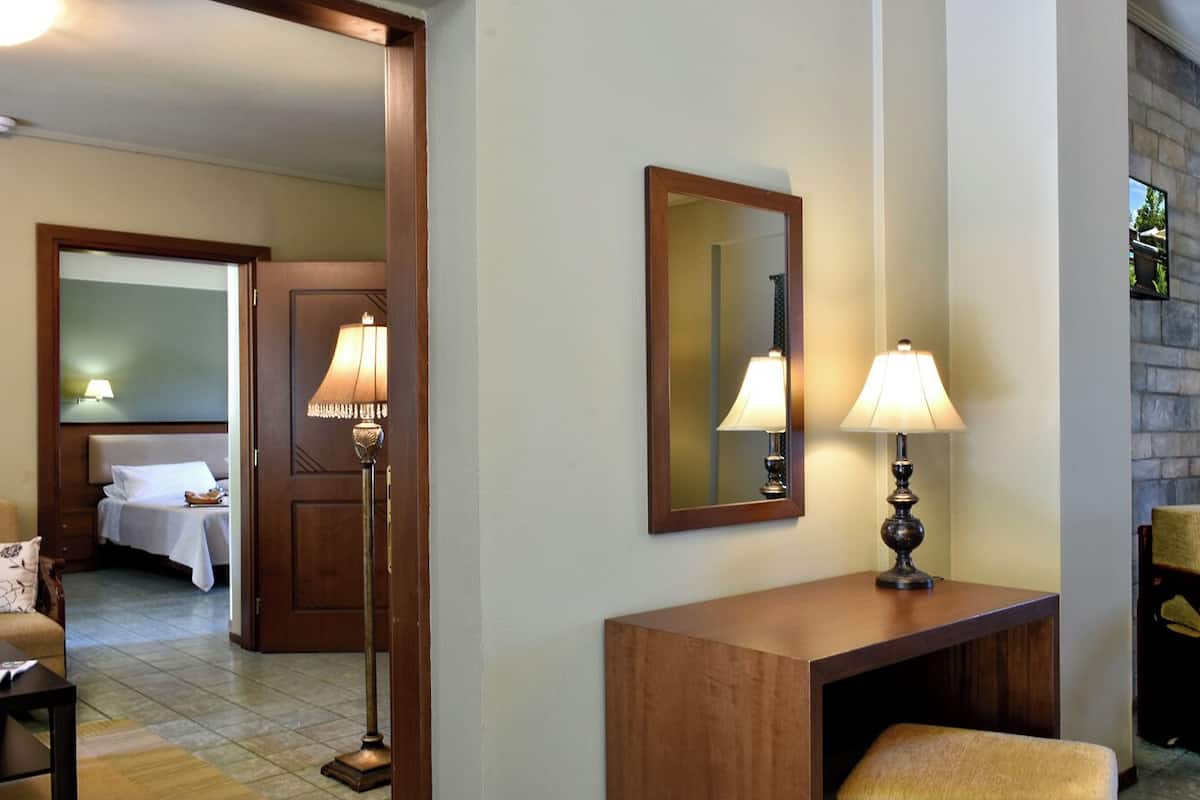 A hotel room with a bed, a desk with a lamp, a chair, and a mirror on the wall.