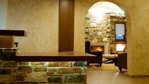 A lobby with a stone reception desk, a fireplace, and a stone wall. - Belina Hotel (Volos)