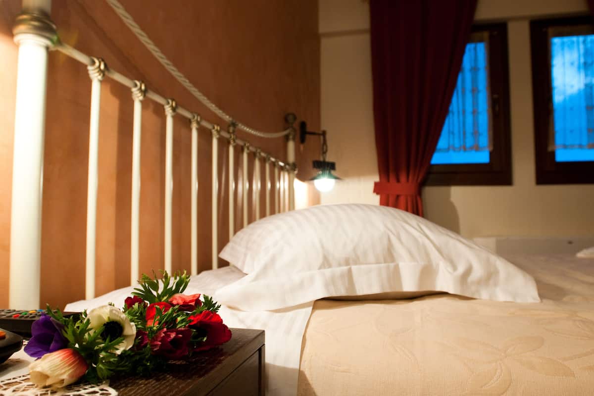 A hotel room with a bed, a nightstand with a lamp, a bouquet of flowers, and a window with curtains.