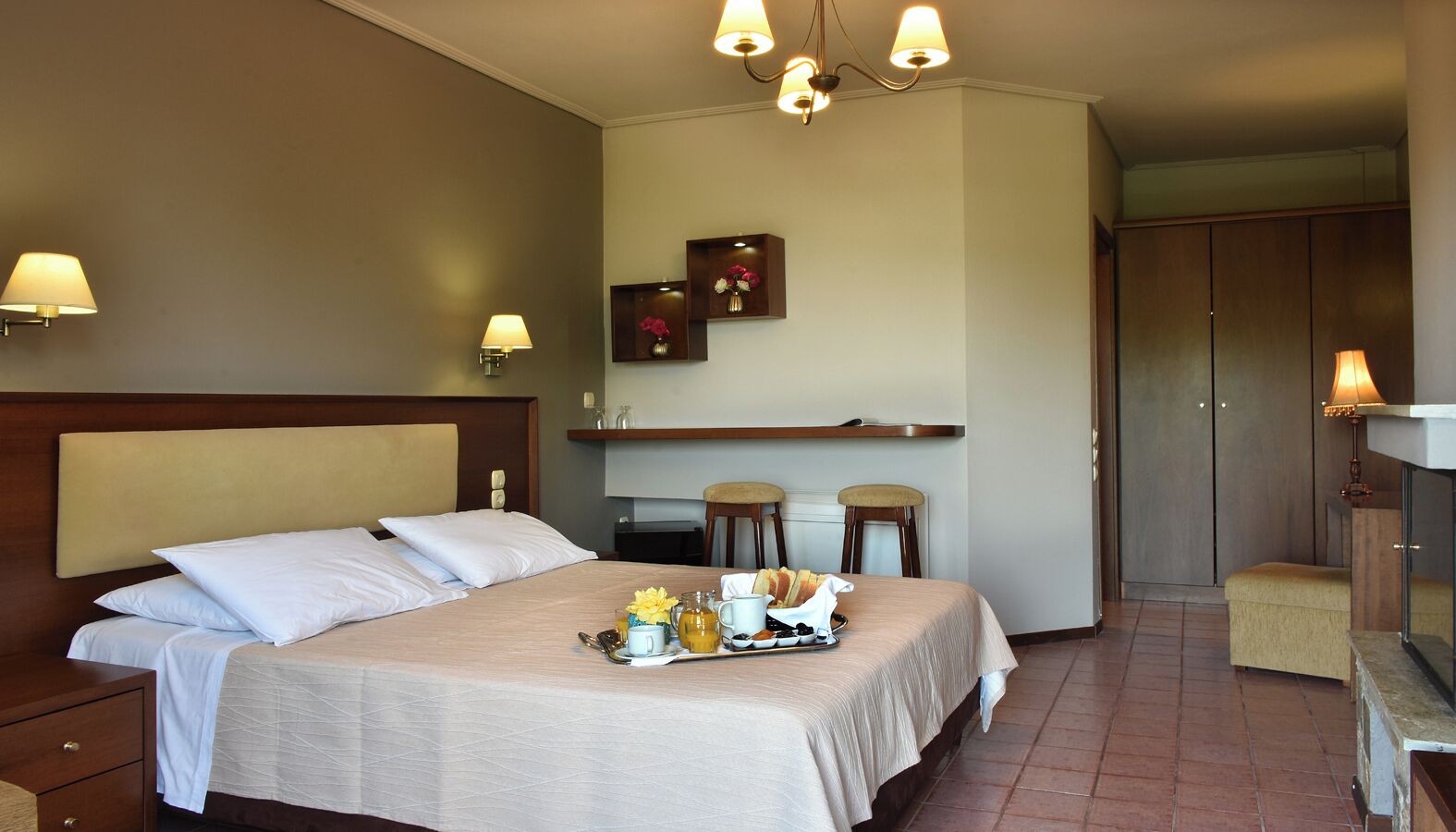 A hotel room with a bed, bedside tables, a small kitchenette, and a seating area.