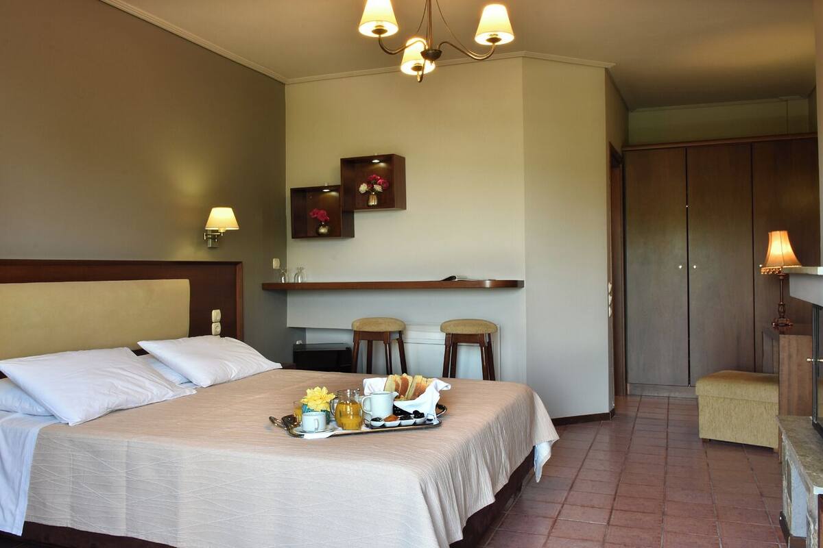 A hotel room with a bed, bedside tables, a small kitchenette, and a seating area.
