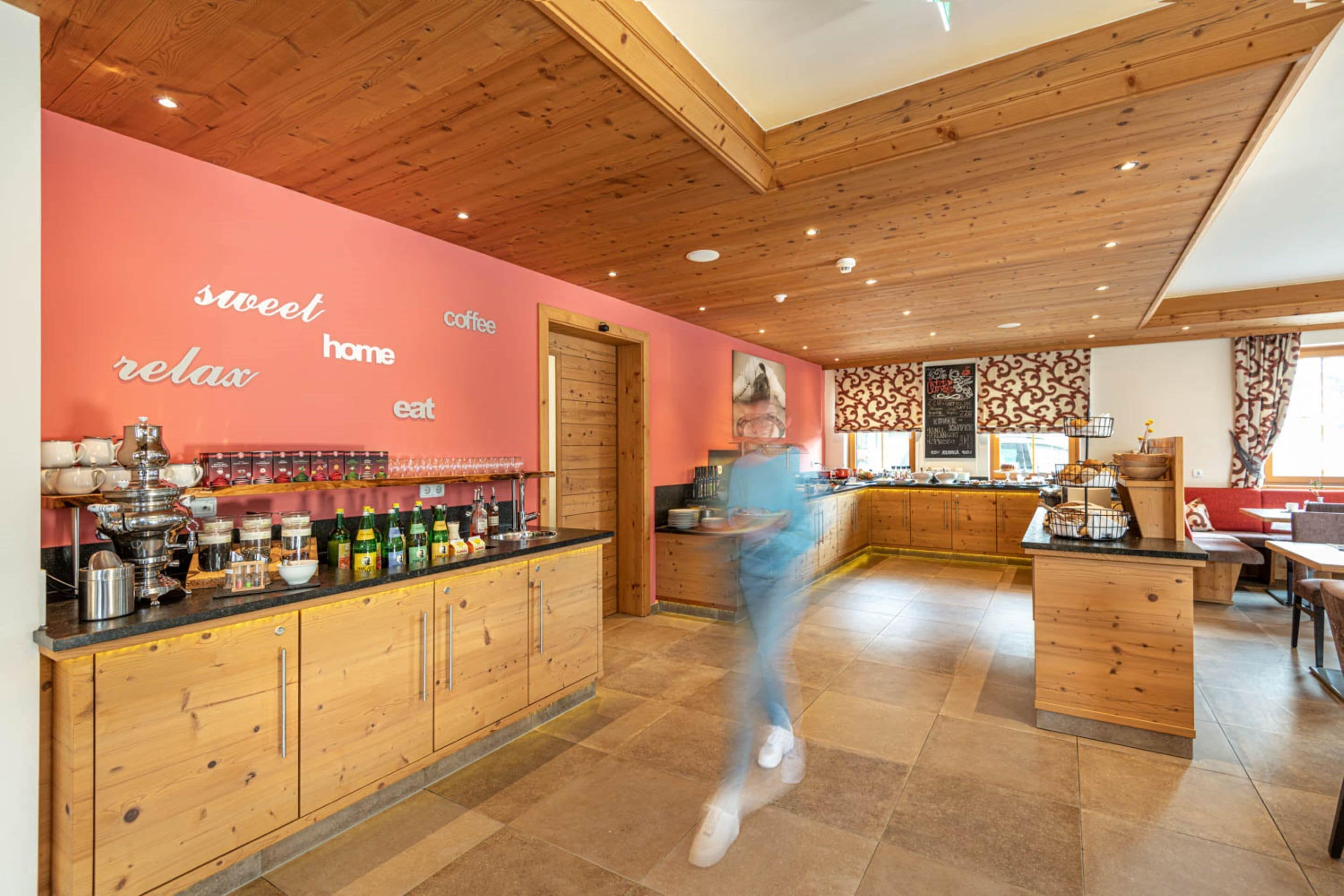 A modern kitchen with wooden cabinets, a black countertop, and a pink wall with motivational words.