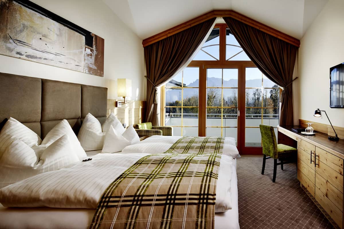 Un dormitorio con una cama grande, un escritorio y vistas a montañas a través de una ventana.