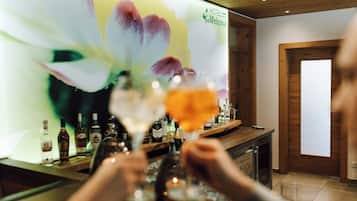 A bar area with a wooden interior, a large floral poster on the wall, and various bottles of alcohol.