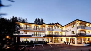 Ein mehrstöckiges Hotel mit einem zentralen Eingang, Balkonen und einem Parkplatz.