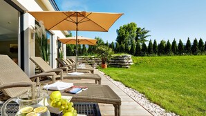Ein Außenbereich mit Korlounge-Stühlen und Sonnenschirmen, ein Tisch mit Zitronenlimonade und Trauben sowie Blick auf einen gepflegten Rasen und Bäume.