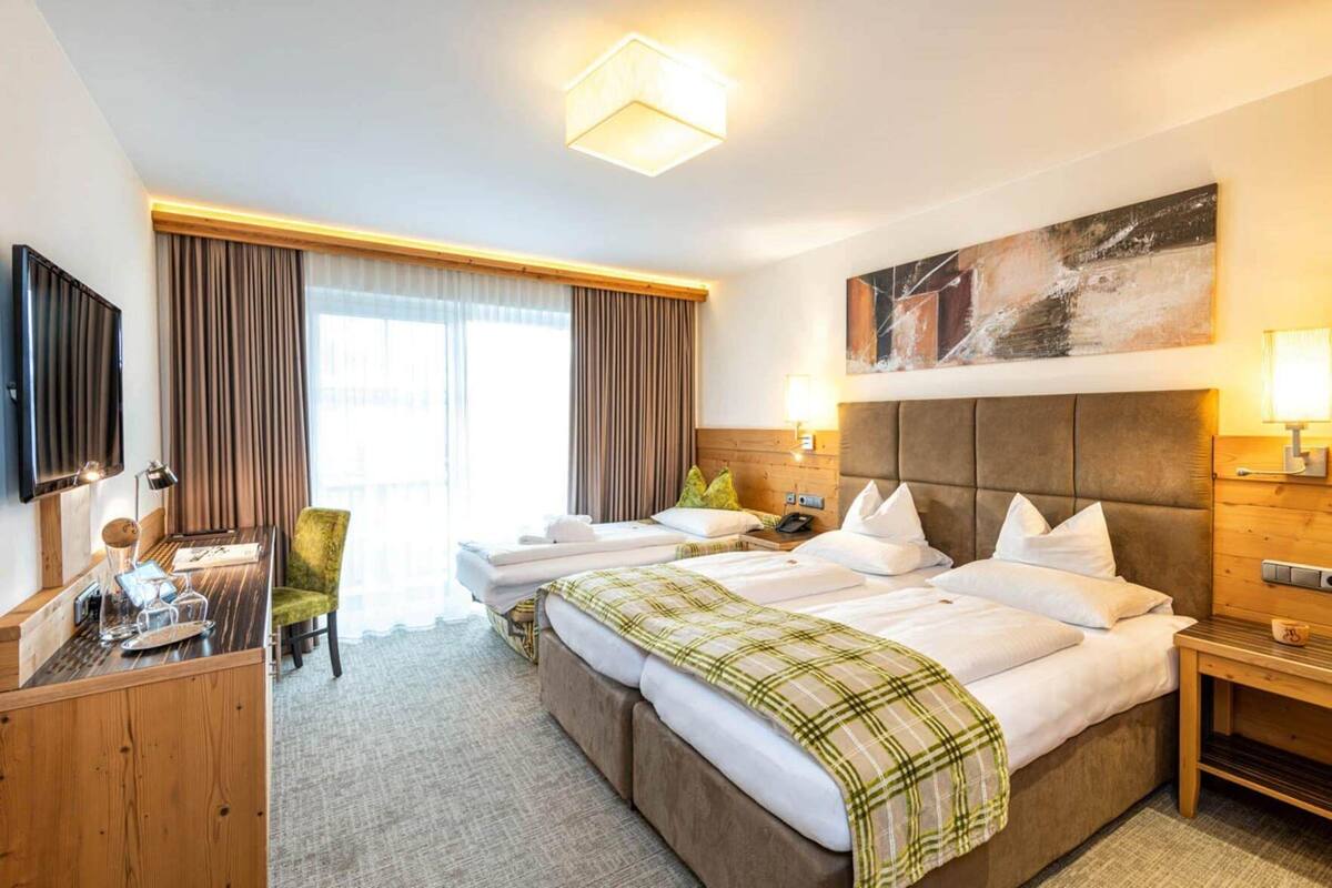Habitación de hotel con una cama grande, un escritorio, una silla, un televisor y un cuadro en la pared.