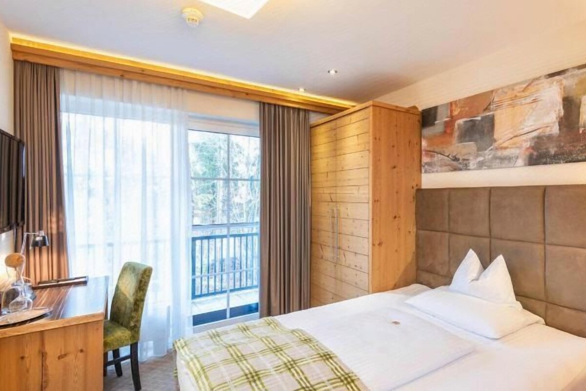 Une chambre d’hôtel avec un lit, un bureau, une chaise, une fenêtre avec des rideaux et un tableau au mur.