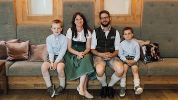 Una familia de cuatro sentada en un banco de madera con respaldo acolchado, en una habitación con paneles de madera y papel tapiz floral.