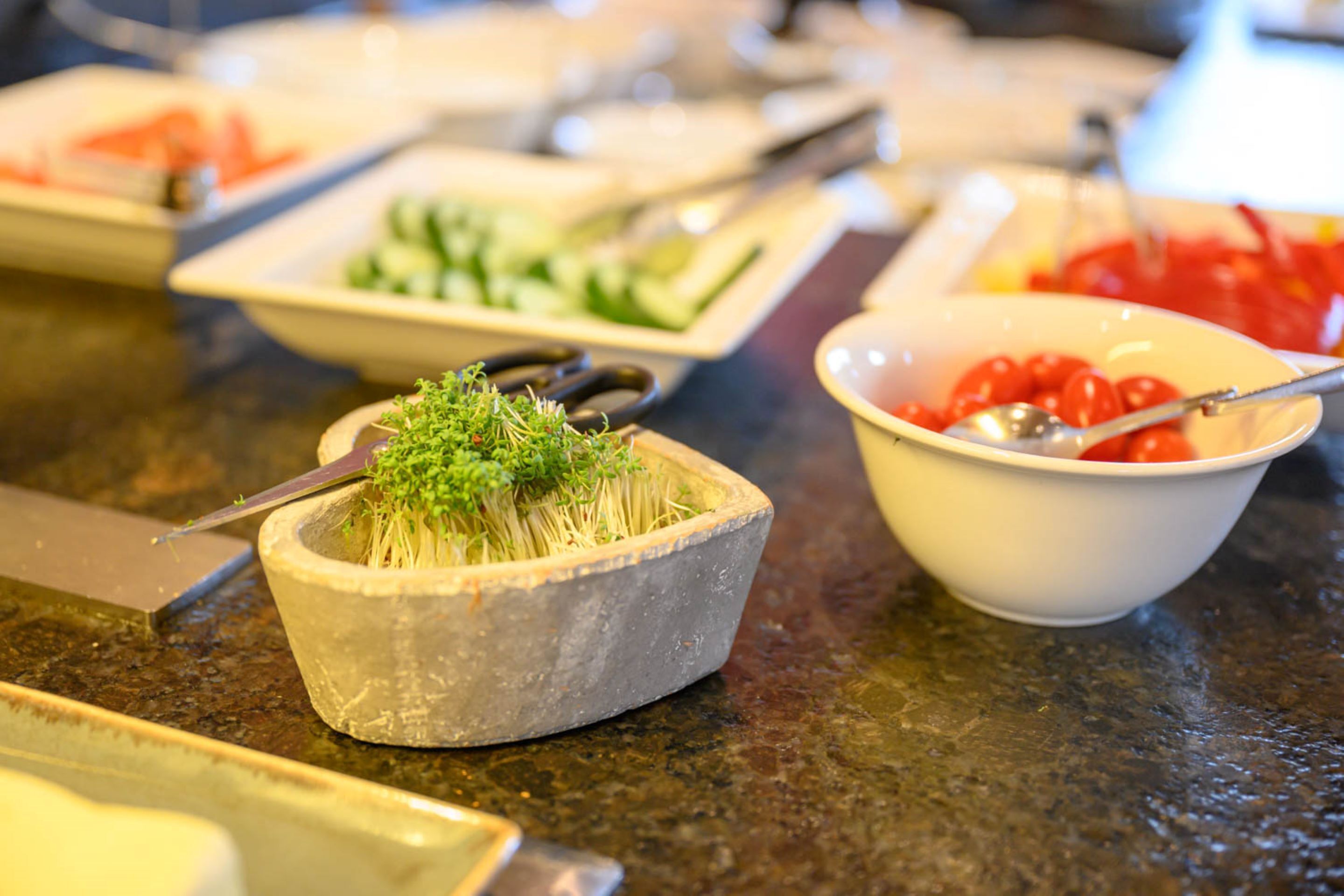 Een buffet met diverse soorten eten, waaronder een schaal spruiten, een schaal kerstomaatjes en een bord met plakjes komkommer.