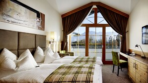 Ein Hotelzimmer mit einem großen Bett, einem Schreibtisch und Blick auf Berge durch das Fenster.
