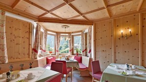 A dining area with wooden paneled walls, a bay window with curtains, and a table set for two.