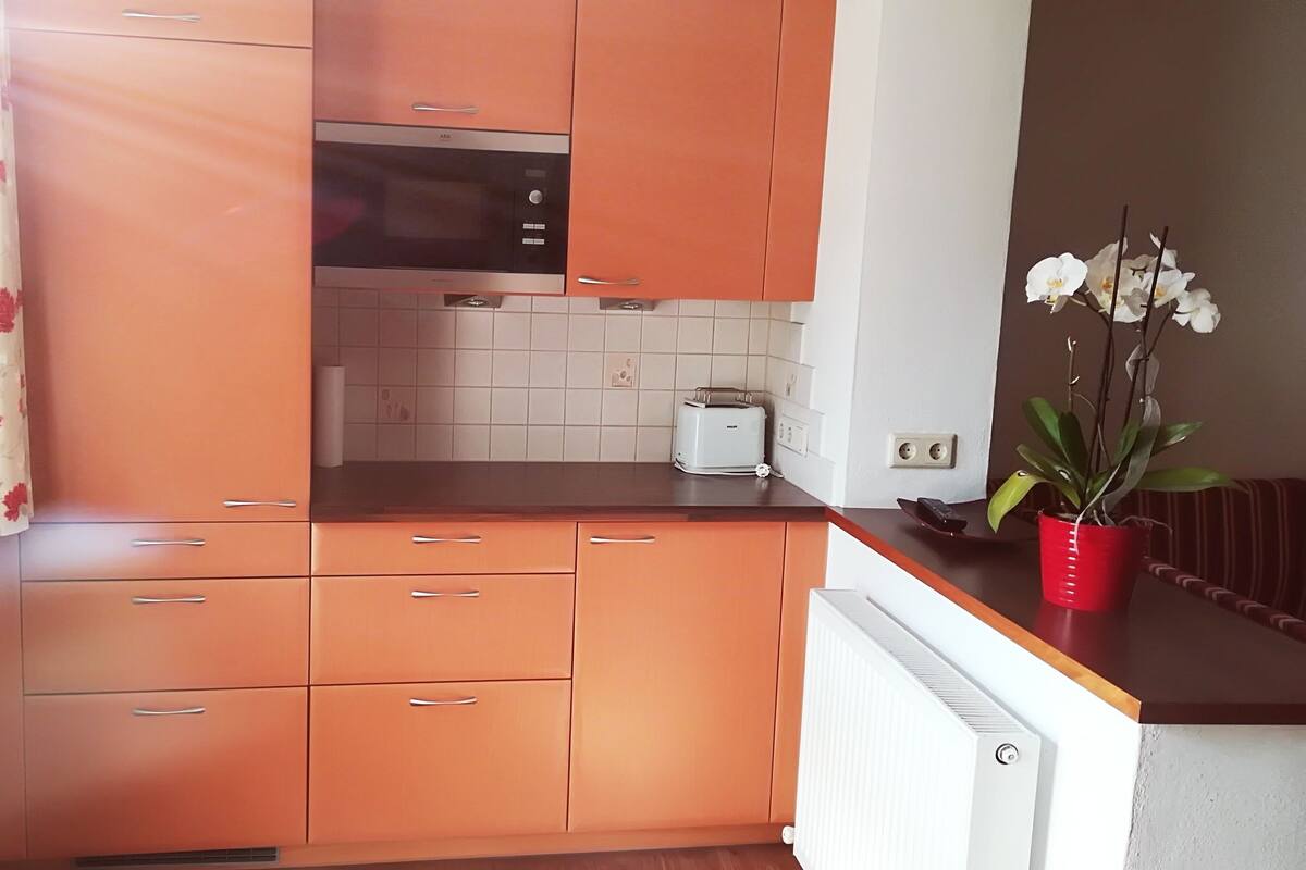 Une cuisine avec des meubles de couleur orange, un four à micro-ondes, un grille-pain et une orchidée en pot.