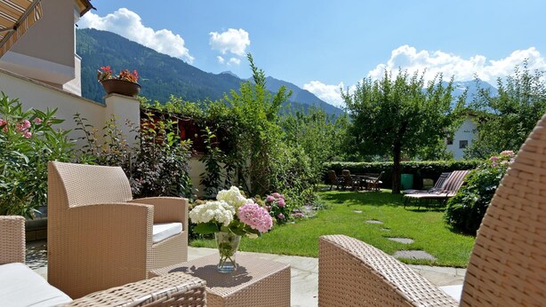 Wicker furniture, a vase with flowers, and a garden with a mountain backdrop.