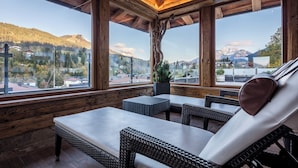 Una habitación con paneles de madera, muebles de mimbre y amplios ventanales con vistas a las montañas.