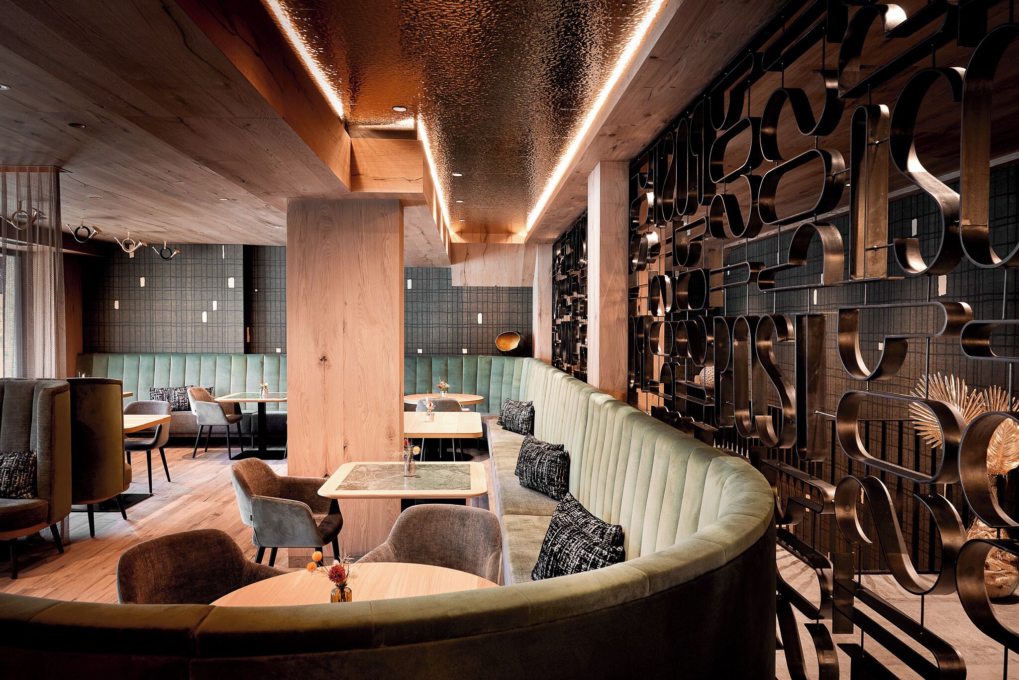 A modern restaurant interior with a curved seating area, wooden accents, and a decorative metal wall.