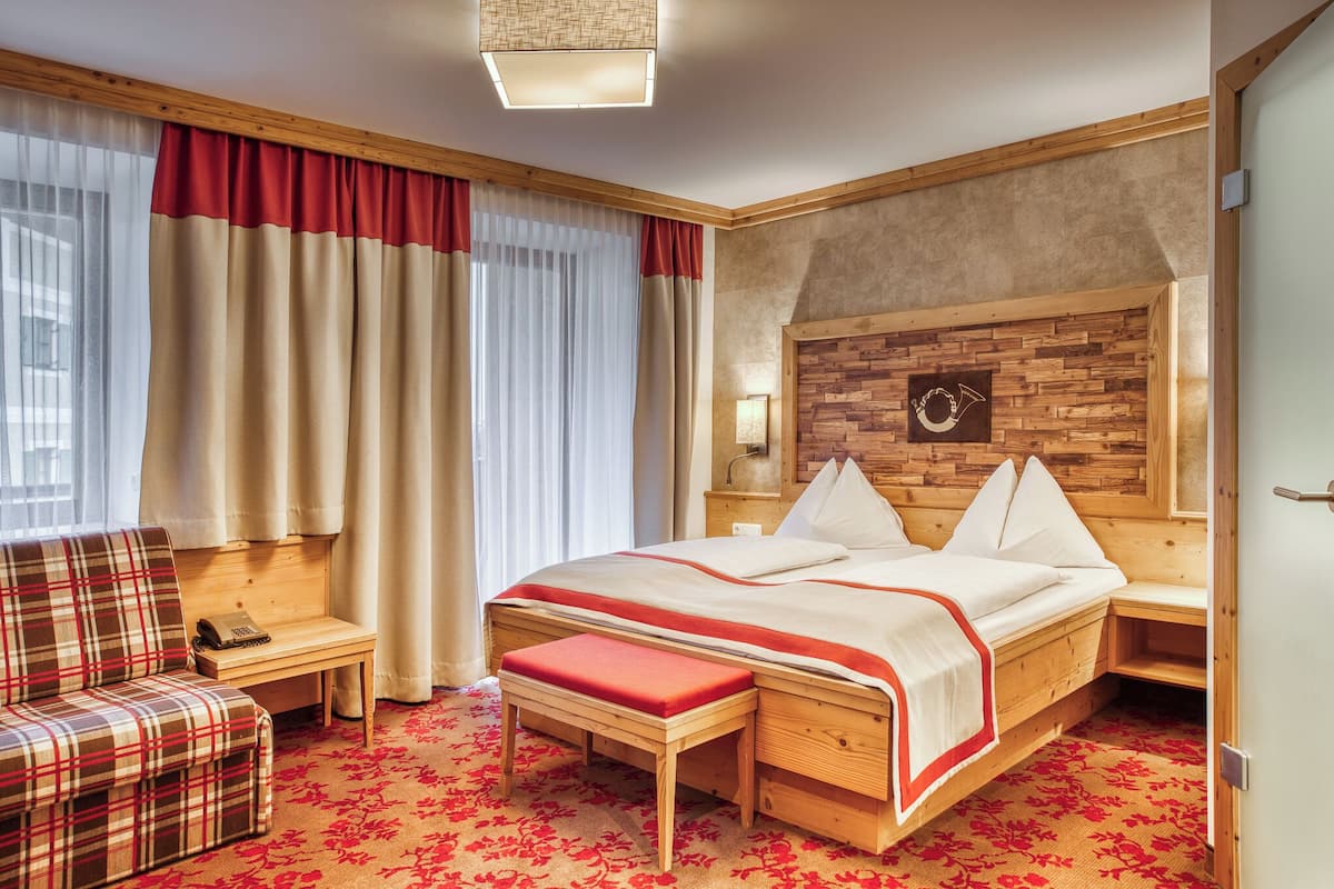 A hotel room with a wooden bed, a bench, a small table, and a chair.