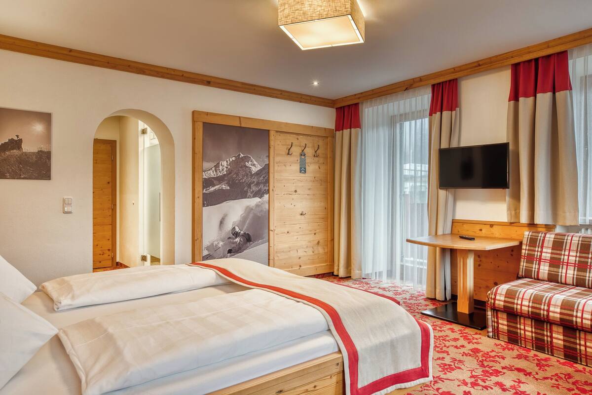 A hotel room with a large bed, a wooden desk, a television, and a sofa.