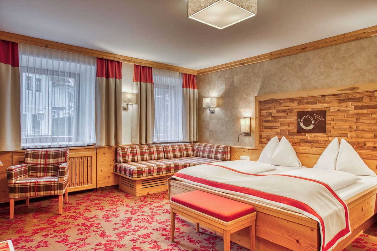 A hotel room with a large bed, a bench, a chair, and a window with curtains.