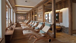 Un área de spa con vigas de madera, paredes de piedra y una fila de tumbonas con cojines.