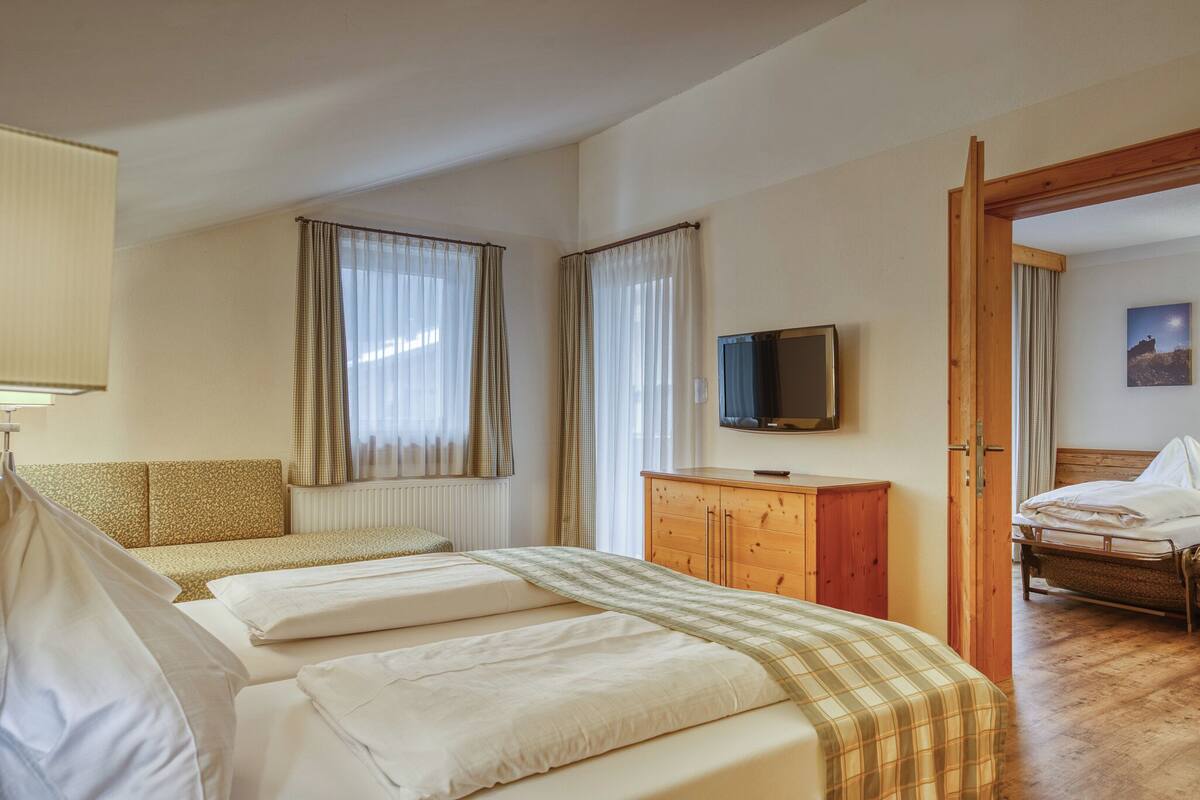 A hotel room with two beds, a wooden cabinet, a television, and a painting on the wall.